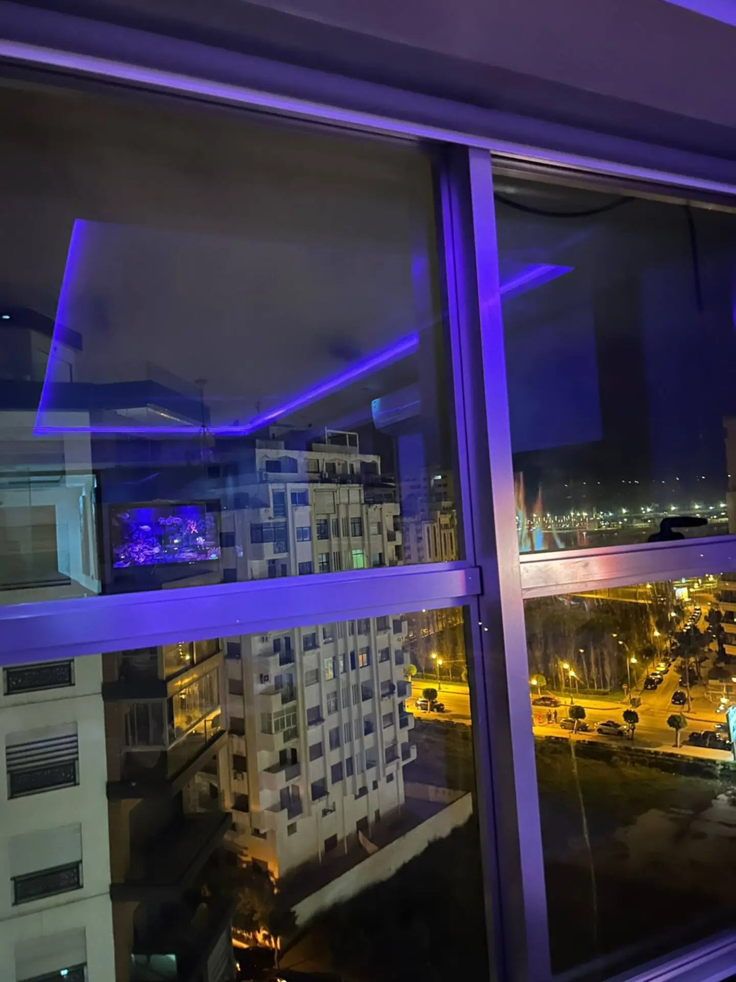 amenagement-entree-luxe-bois-miroir-luminaire-led Console flottante en bois sur mur en tasseaux, grand miroir rond et éclairage LED rouge dans un appartement moderne.