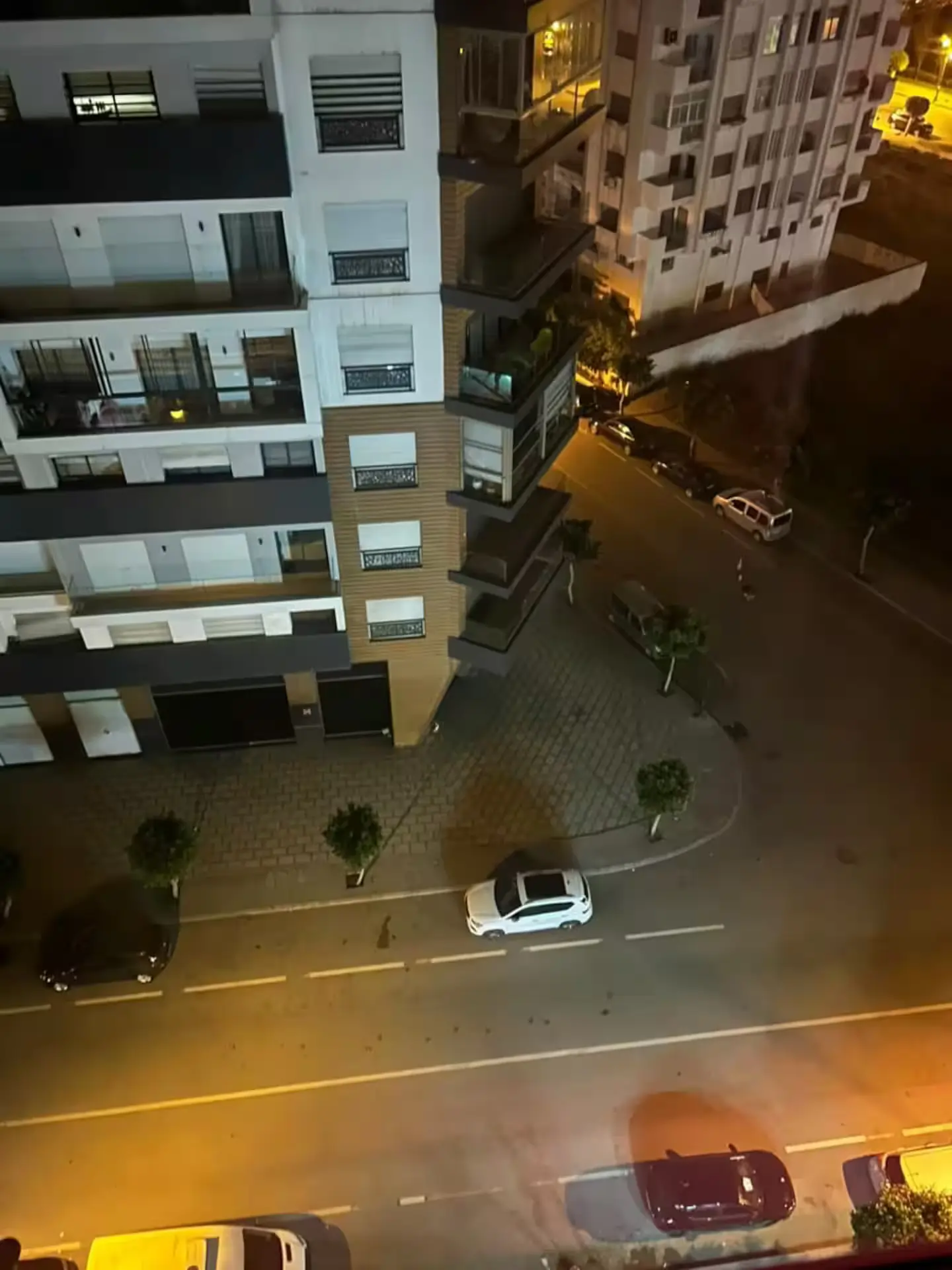 appartement-luxe-moderne-vue-nuit-ville Vue plongeante de nuit sur une résidence immobilière de luxe au design contemporain avec balcons vitrés et rue éclairée.