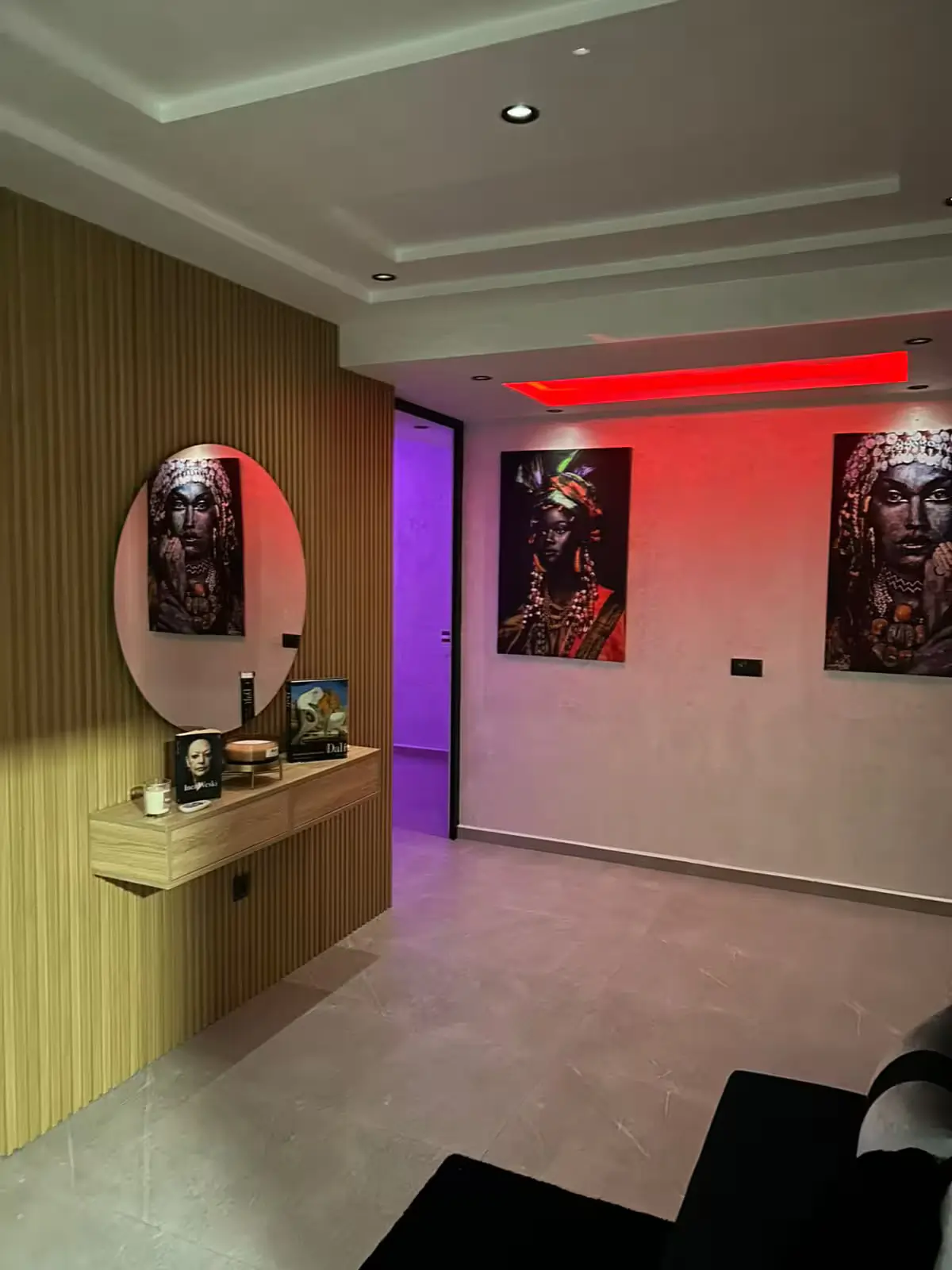 entree-luxe-moderne-parement-bois-eclairage-rouge Entrée d'appartement moderne avec mur en tasseaux de bois, miroir rond, console suspendue et tableaux d'art africain sous un éclairage LED rouge