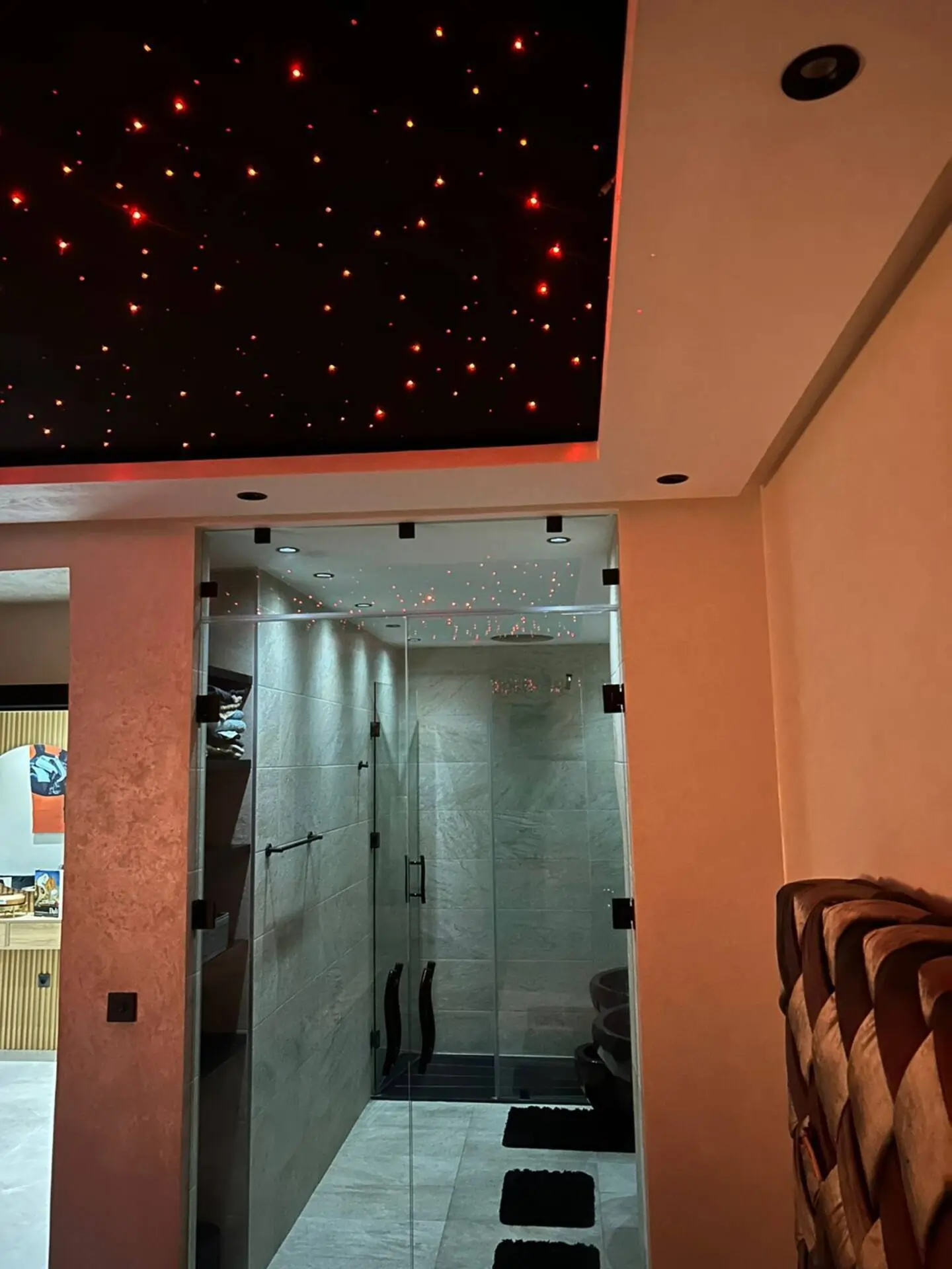 suite-parentale-luxe-plafond-etoile-salle-de-bain Suite parentale de luxe avec plafond étoilé à fibre optique rouge et salle d'eau moderne vitrée.