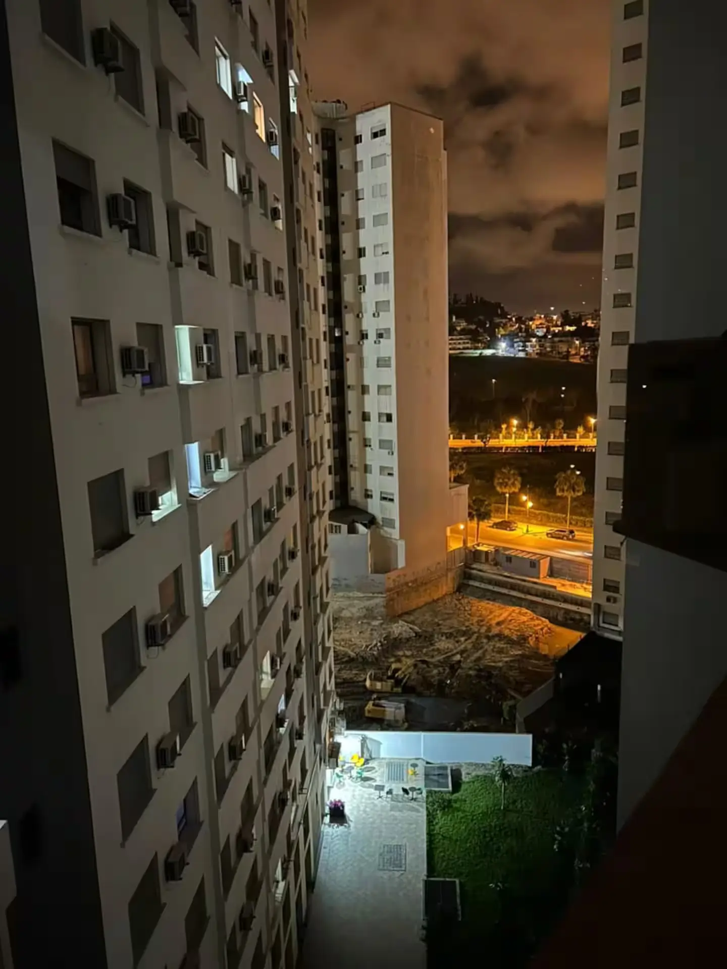 vue-balcon-appartement-luxe-ville-nuit Vue nocturne depuis le balcon d'un appartement de grande hauteur montrant les lumières de la ville et les immeubles modernes.